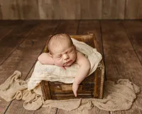 Sleeping newborn baby posed with arms resting over the edge of a wooden crate on a soft cream blanket during a classic studio newborn photography session photographed by Kaitlyn Dawn Photography.