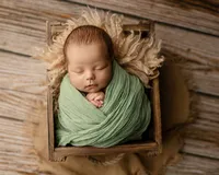 Sleeping newborn baby boy wrapped in a green swaddle and posed in a rustic wooden crate during a studio newborn photography session by Inland Empire newborn photographer Kaitlyn Dawn Photography.