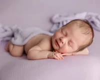 Smiling newborn baby resting on a soft lavender blanket with hands tucked under the chin during a natural light newborn photography session by Kaitlyn Dawn Photography.
