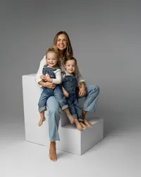 Mother sitting on white studio blocks cuddling her two toddlers, soft neutral tones and modern studio styling by Kaitlyn Dawn Photography, professional family photographer.