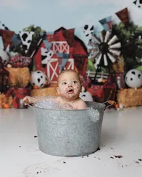 Little boy sitting in a bubbly metal tub with cake still on his face, in front of a rustic barn-themed backdrop.
Photograph by Yucaipa cake smash photographer Kaitlyn Dawn Photography.