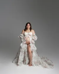 Pregnant woman smiling in a floral maternity gown during a soft studio maternity photography portrait by Kaitlyn Dawn Photography.
