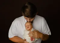 Father gently kissing his newborn baby during a cozy family portrait. Photographed by Inland Empire newborn photographer Kaitlyn Dawn Photography.