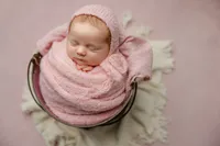 Sleeping newborn baby girl wrapped in a soft pink swaddle and posed on a neutral textured blanket during a studio newborn portrait with newborn photographer Kaitlyn Dawn Photography.