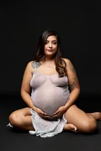 Elegant pregnancy portrait of a pregnant woman sitting on the studio floor wearing a soft textured maternity dress photographed by Kaitlyn Dawn Photography.
