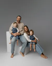 Family of four sitting together on white studio cubes with soft gray background, coordinated neutral outfits captured by Kaitlyn Dawn Photography, studio family photographer in Inland Empire.