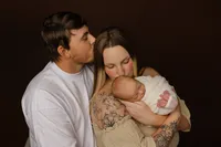Family portrait of parents embracing their newborn baby with warm expressions. Photographed by Inland Empire newborn photographer Kaitlyn Dawn Photography.