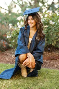 High school graduate posing outdoors in a blue cap and gown during golden hour, senior photography by Kaitlyn Dawn Photography.
