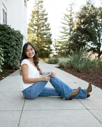 High school senior girl sitting on a paved walkway with trees and greenery in the background, outdoor senior portrait by Kaitlyn Dawn Photography.