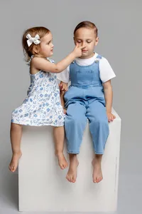 Brother and sister sitting together on a white studio cube in a minimalist gray studio, playful and candid sibling portrait by Kaitlyn Dawn Photography, professional family photography studio.