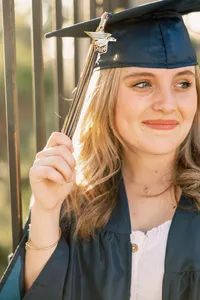 Close-up portrait of a smiling high school graduate wearing a cap and gown, golden hour graduation photography by Kaitlyn Dawn Photography.