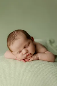 Sleeping newborn baby posed on a soft green backdrop during a studio newborn photography session with newborn photographer Kaitlyn Dawn Photography.