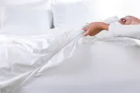 woman's hand in corner of image pulling white sheets over the bed