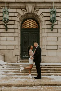Newlyweds kissing on the snow-covered steps outside the historic Cuyahoga County Courthouse building in downtown Cleveland during their winter elopement portrait session.