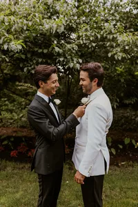 Wedding day portrait featuring two grooms in formal attire sharing a candid moment in a garden setting.