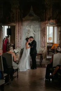 Bride and groom share their first kiss during intimate Italy destination wedding ceremony in ornate venue.