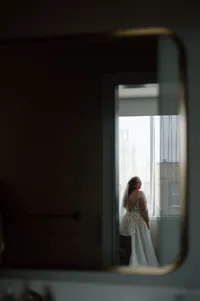Bride in wedding gown looks out city window before wedding ceremony during quiet candid moment.