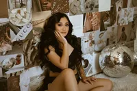 A woman with long dark hair sits on a plush bed beside a disco ball, surrounded by a warm-toned collage of fashion, beauty, and luxury images.