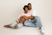 smiling expecting couple holding each other tenderly in studio portrait for maternity photoshoot