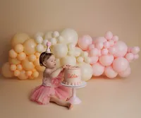 baby touching cake with orange, yellow, and pink balloons in the background during milestone portrait session at CG Photography North Hollywood