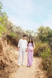 candid moment of expecting couple surrounded by foliage holding hands during outdoor maternity photoshoot in Los Angeles