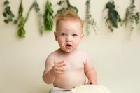 baby sitting up with cake frosting on his face during milestone portrait session at CG Photography Los Angeles