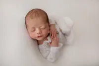 sleeping newborn in white onesie on white backdrop during luxury newborn session in Los Angeles