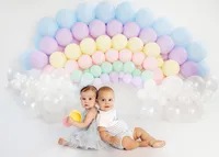 two babies sitting back to back with rainbow balloon arch during milestone portrait session in Burbank