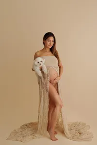 expecting mother in gown revealing baby bump holding her dog during artistic studio Los Angeles maternity portrait