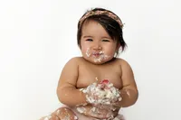 baby clapping hands and smiling with cake during joyful milestone photography session in Los Angeles