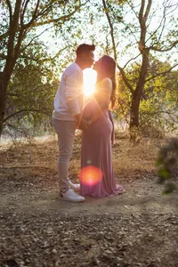 expecting couple during golden hour surrounded by foliage kissing each other holding hands during outdoor maternity photoshoot in Los Angeles