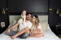 in-home portrait of smiling family in bed with newborn baby