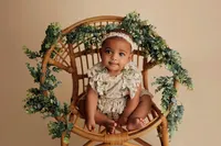 newborn baby in posed position in chair with green foliage prop during luxury studio session in Los Angeles