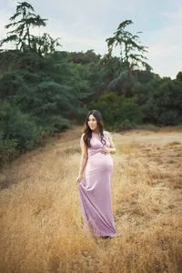 expecting mother in gown smiling holding baby bump during outdoor maternity session in Los Angeles surrounded by trees