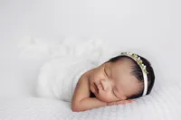 newborn in soft white wrap with floral headband during elegant studio portrait session in North Hollywood