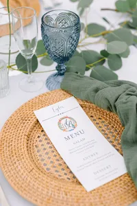 Place setting with a rattan charger, blue glassware and menu