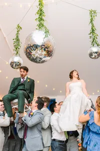 Groom lifted on a chair during a lively celebration under disco balls
