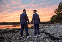 Grooms holding hands on the shoreline at sunset