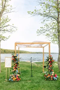 Wooden ceremony arbor with bright floral arrangements by the water