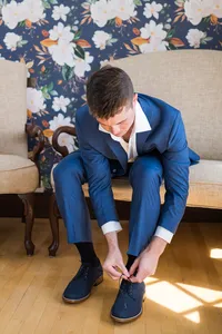 Groom in a navy suit tying his dress shoes while getting ready at French's Point