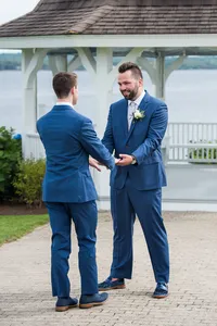 Jimmy and Alex smiling at each other in matching navy suits during their first look at French's Point