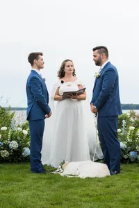 Jimmy and Alex exchanging vows with their officiant beside white hydrangea arrangements at their French's Point ceremony