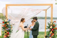 Bride and groom exchange vows under a wooden arbor overlooking Penobscot Bay