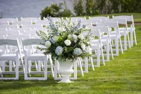 White hydrangea and greenery urn arrangement beside white ceremony chairs on the lawn at French's Point