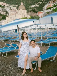 Engagement session on Positano beach with a couple posing under blue umbrellas — romantic and editorial destination photography.