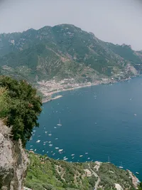 Aerial view of the Amalfi Coast with mountains and boats dotting the blue sea — a breathtaking setting for luxury destination weddings in Italy.