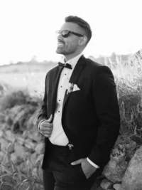 Groom in black tuxedo smiling during golden hour – timeless Italy wedding photography portrait.