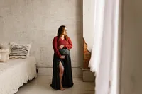 an expecting mom cradles her belly while looking out a windle during her maternity session with shelly voss.