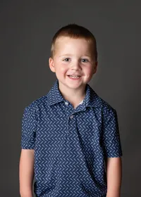 A happy kindergarten boy smiling widely for his school photo.