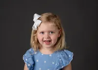 A cute young girl wearing a blue dress and smiling for her school photo.